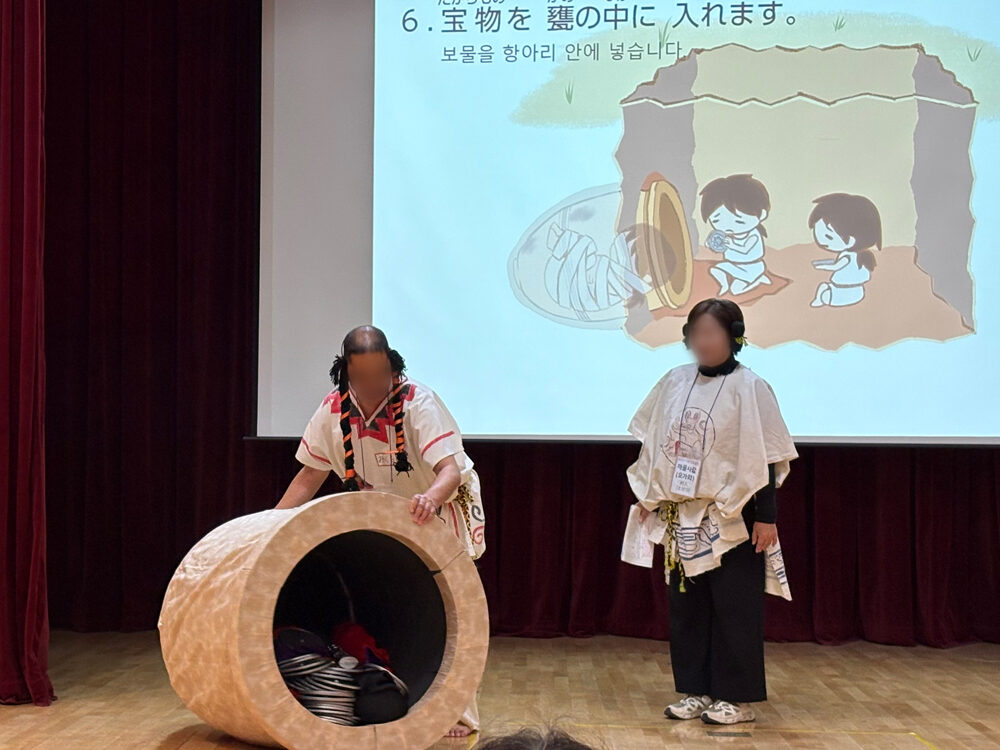 王様を入れた甕棺に副葬品を入れる様子